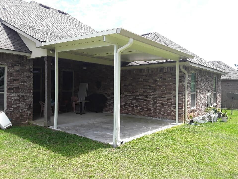 There is a covered patio in the backyard of a brick house.