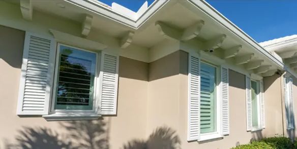 A house with white shutters on the windows and a blue sky in the background.