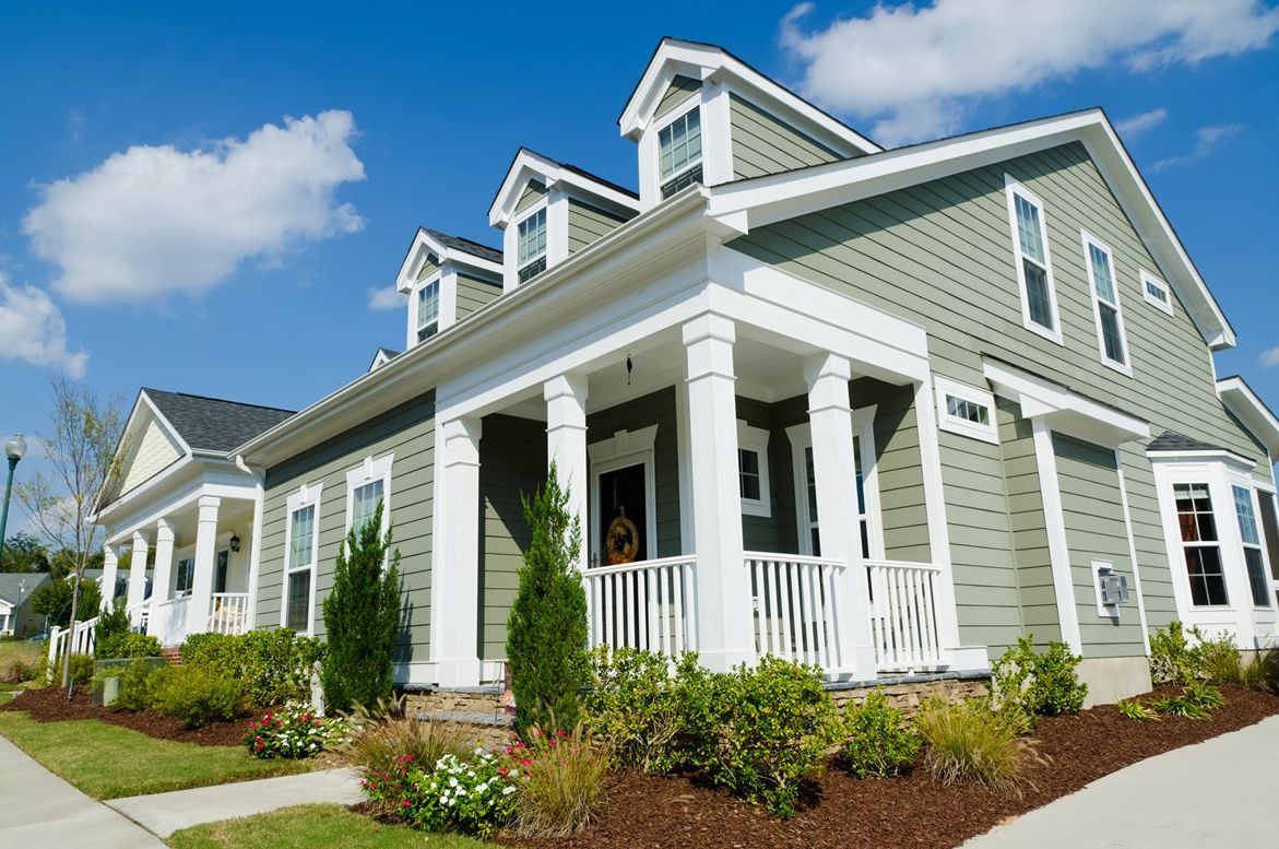 A green and white house with a porch on a sunny day.