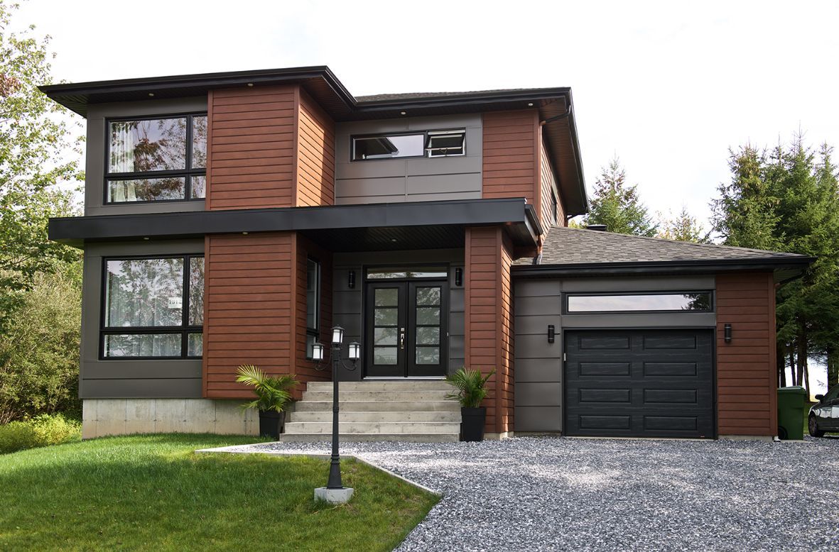 A modern house with a black garage door is sitting on top of a lush green hillside.