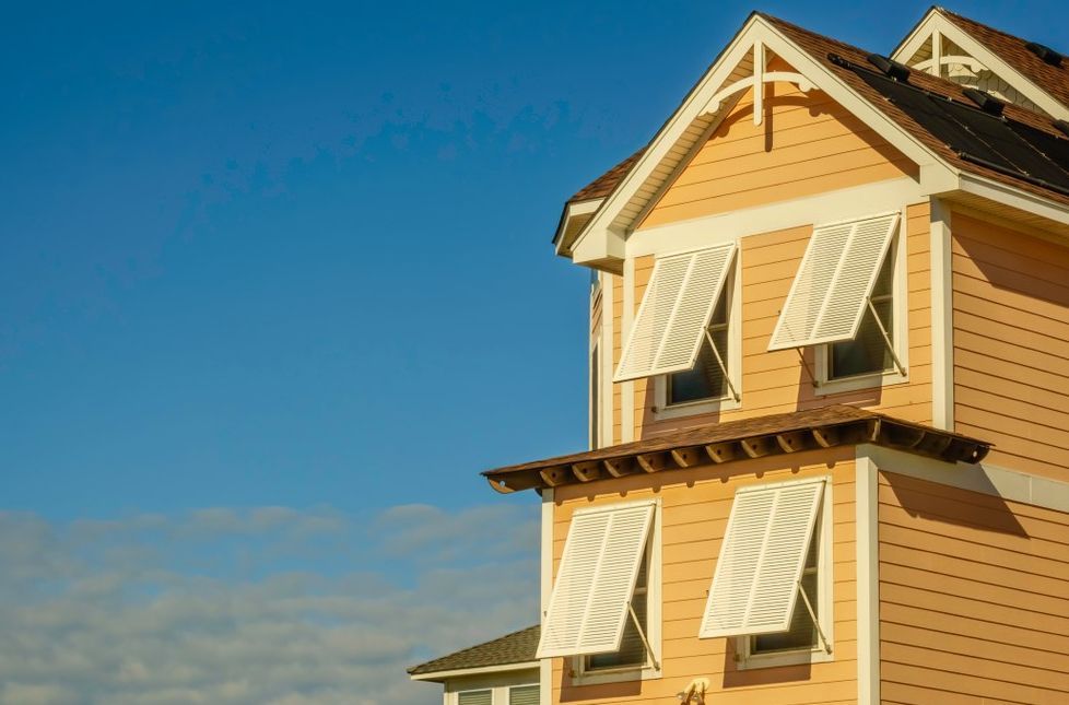 A yellow house with white shutters on the windows against a blue sky.