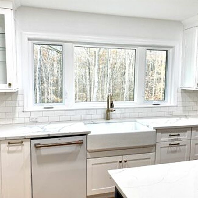 A kitchen with white cabinets, a sink, a dishwasher, and a large window.