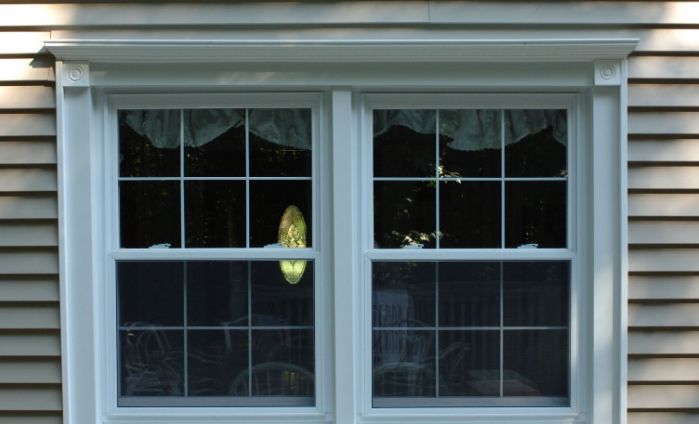 A white window with a white trim sits on the side of a house.