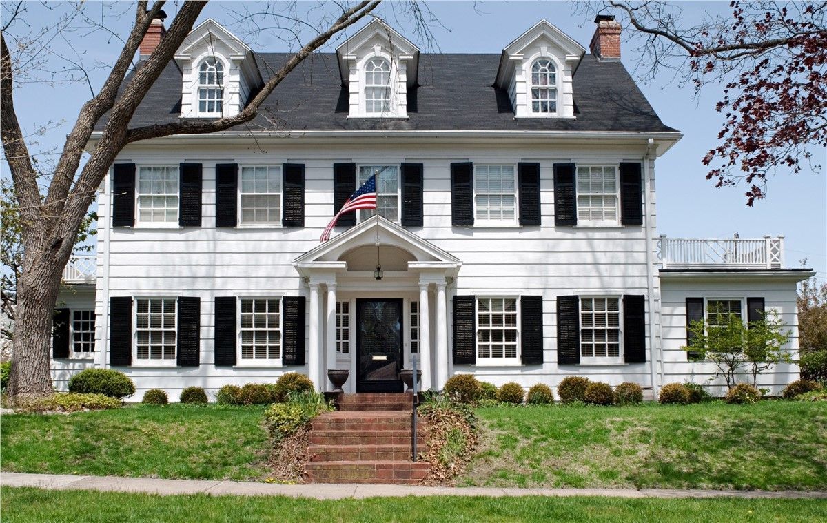 A large white house with black shutters and an american flag
