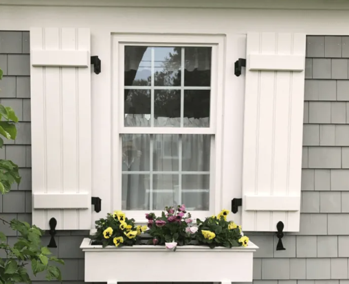 A window with white shutters and flowers in a window box