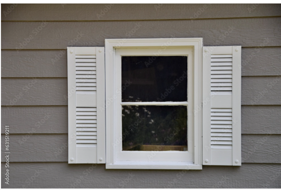 A window with white shutters on the side of a house