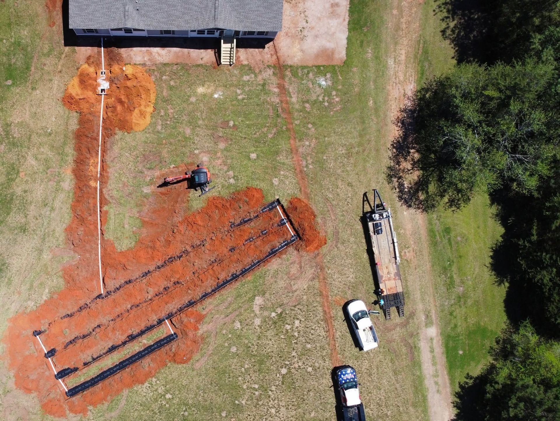 Aerial view of workers installing orange roofing tiles beside a building, with equipment and parked vehicles nearby