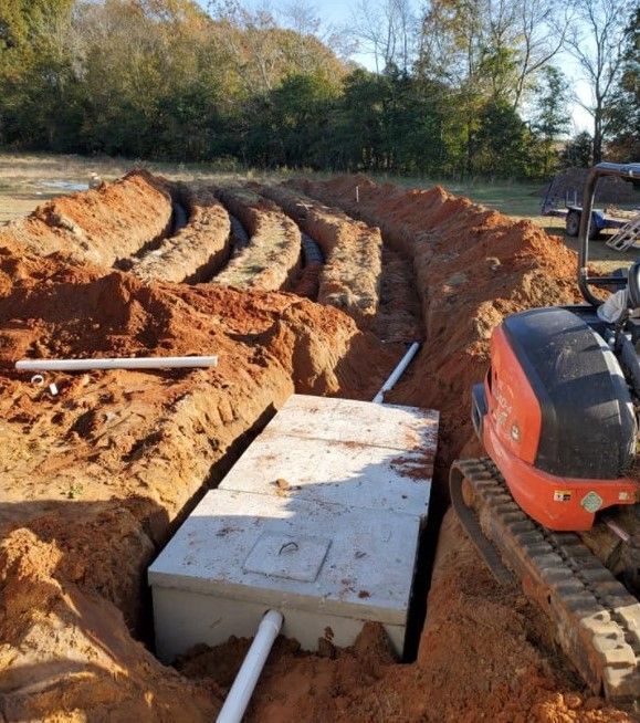 Excavator beside a deep trench with concrete footings and white pipes at a construction site