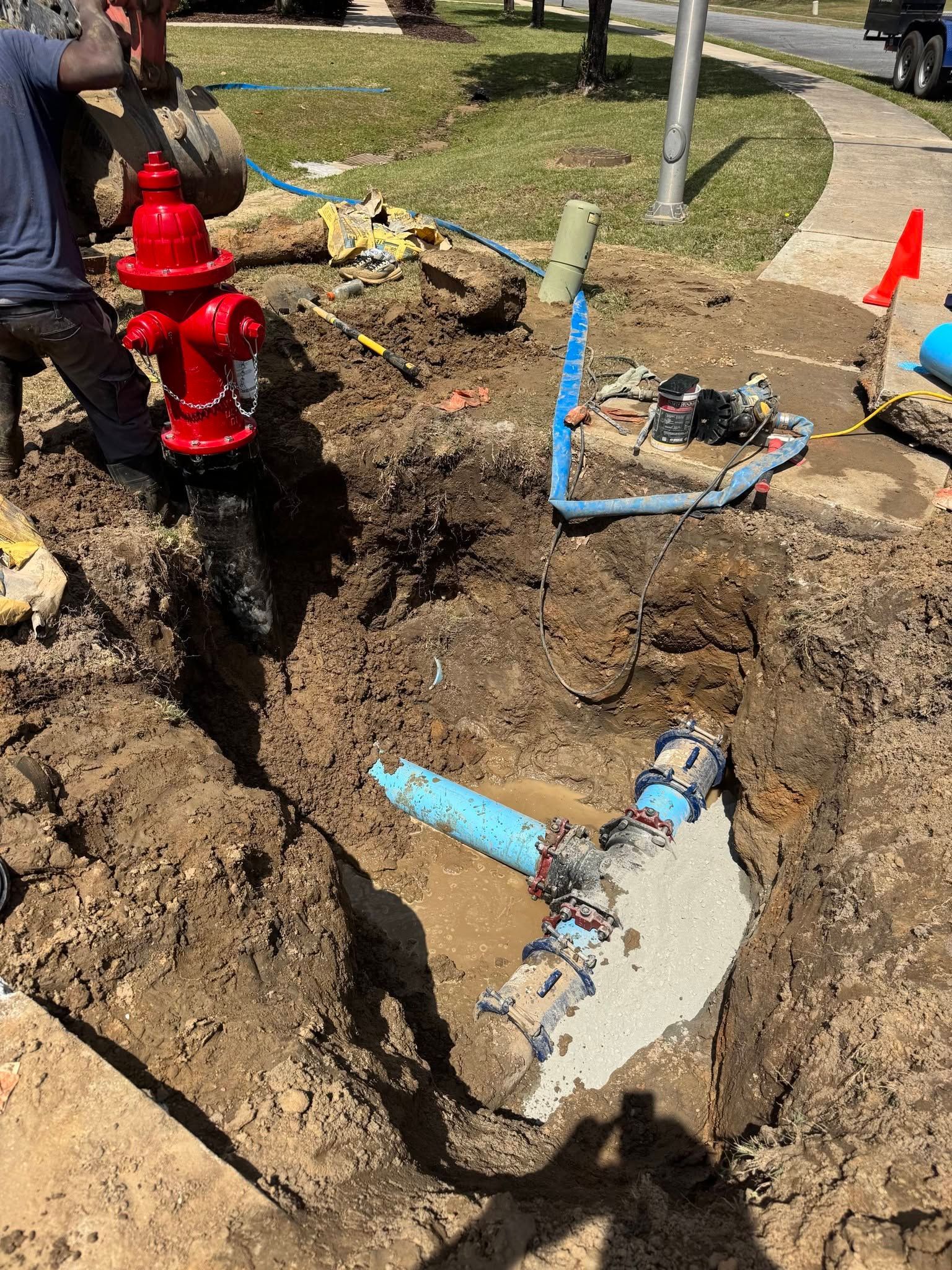 Damaged blue water pipe and red fire hydrant exposed in a muddy roadside excavation