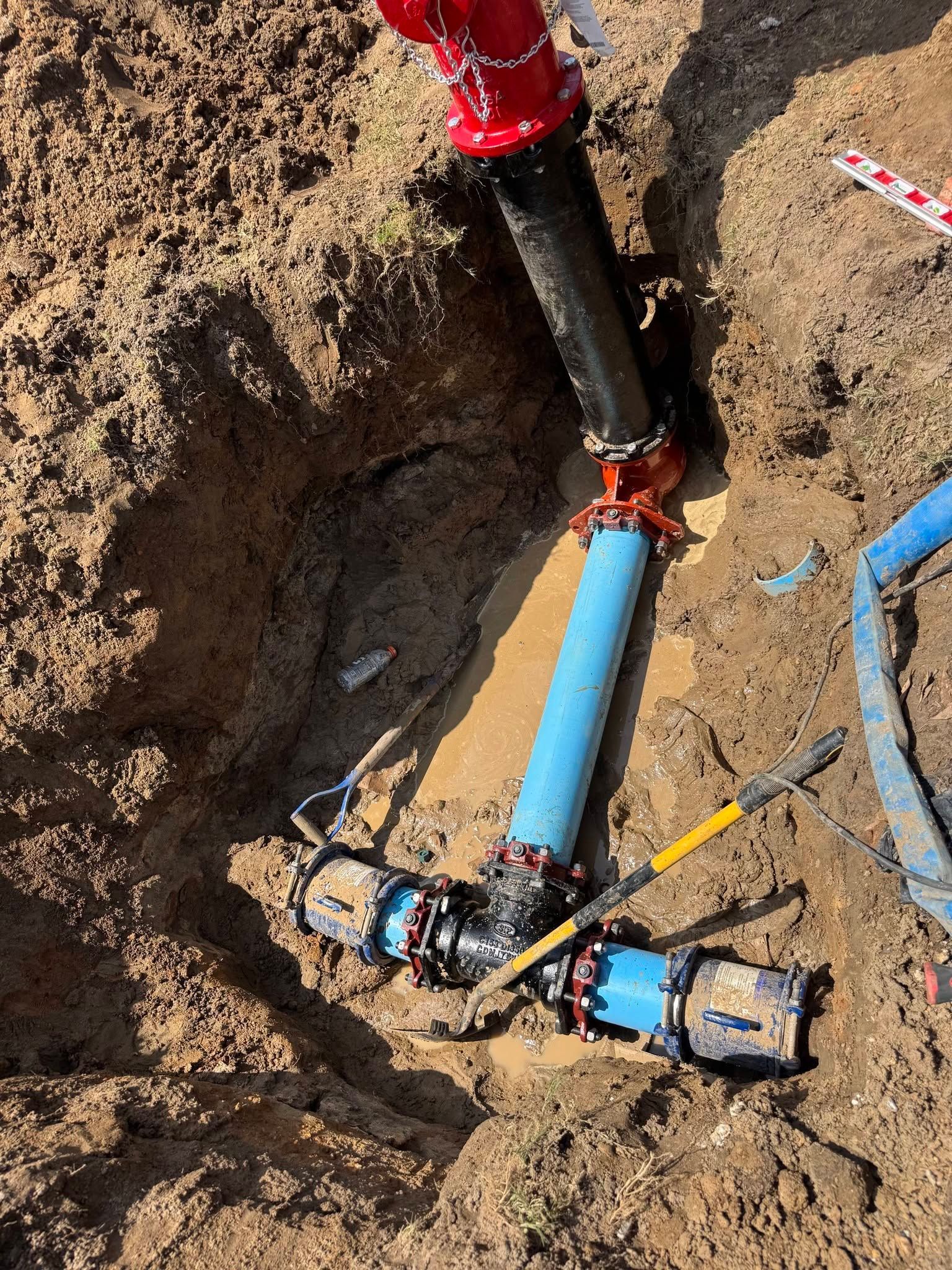 Utility pipe repair in a dirt trench with blue and black pipes and red equipment attached