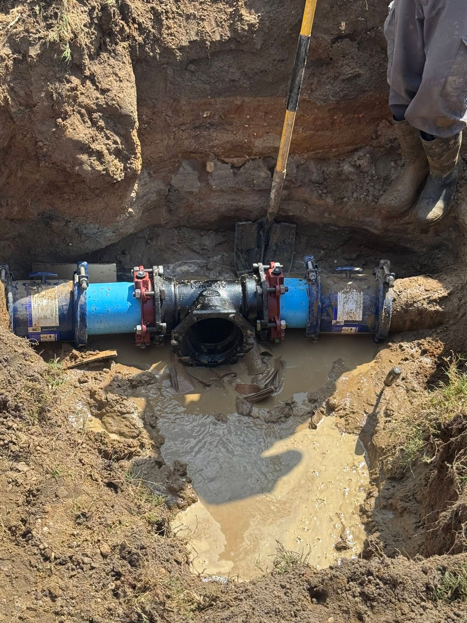 Workers repairing a blue pipeline in a muddy trench with an exposed central valve section