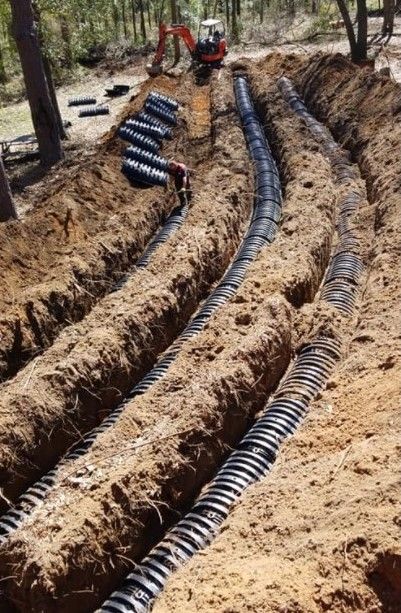 Trenches in a wooded area with black corrugated pipes laid for underground utility installation