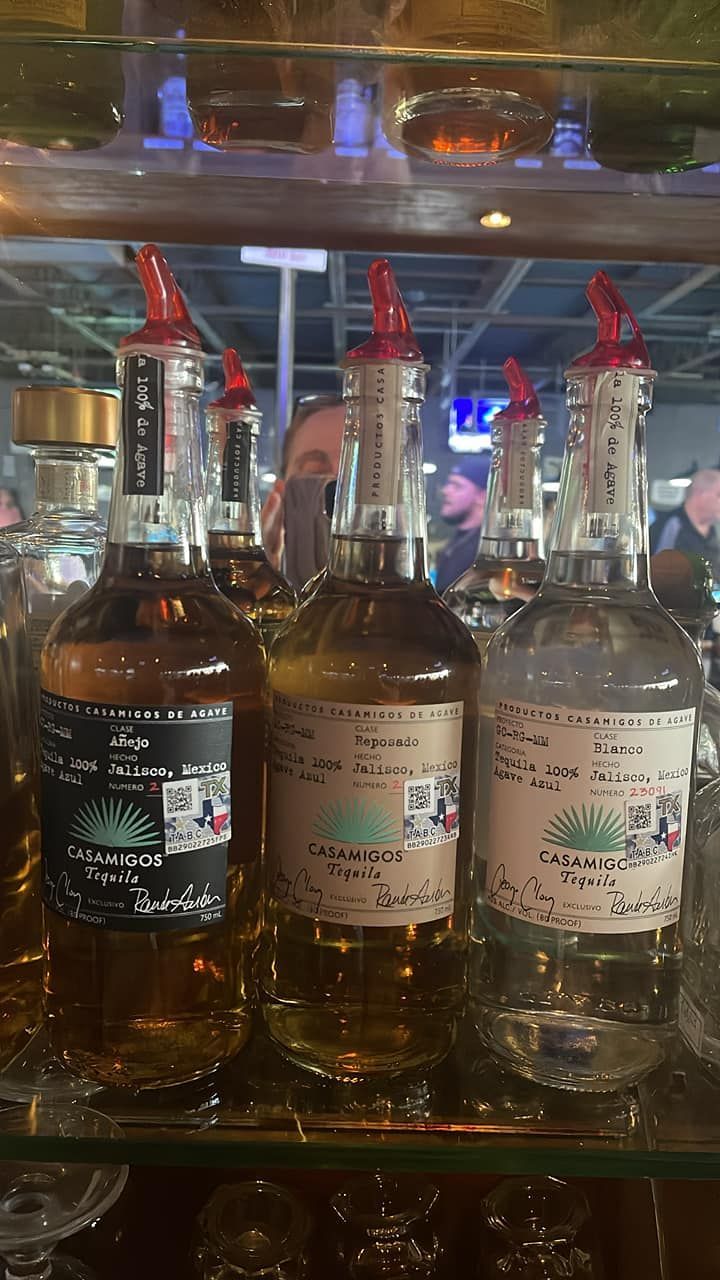 Three bottles of tequila are sitting on a glass shelf in a bar.