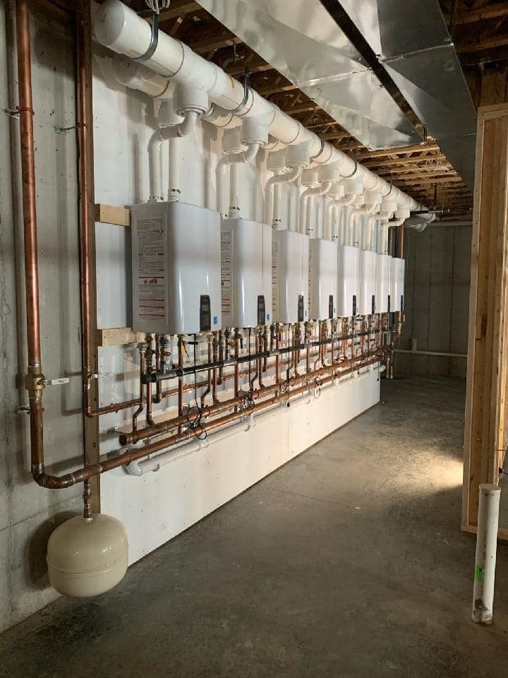 A row of water heaters are lined up on a wall in a basement.