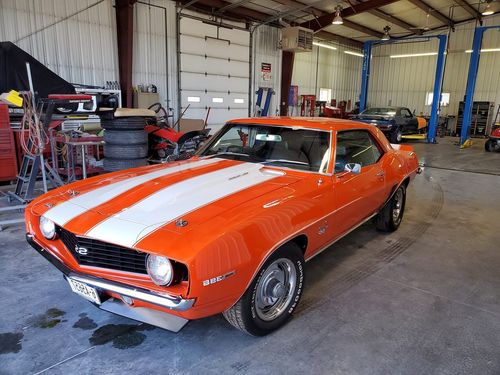 Orange classic muscle car with white racing stripes parked inside a garage.