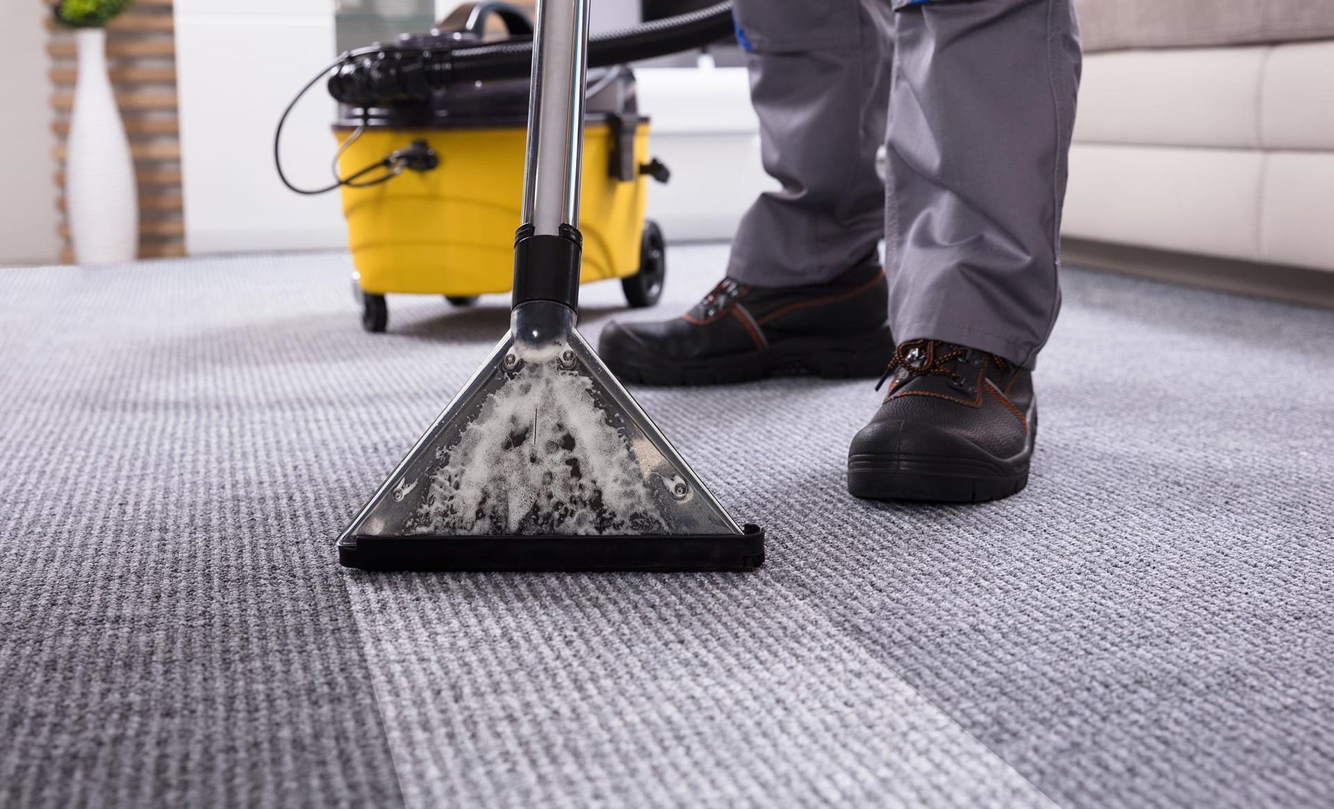 Person cleaning a gray carpet with a yellow carpet cleaner, indoors.