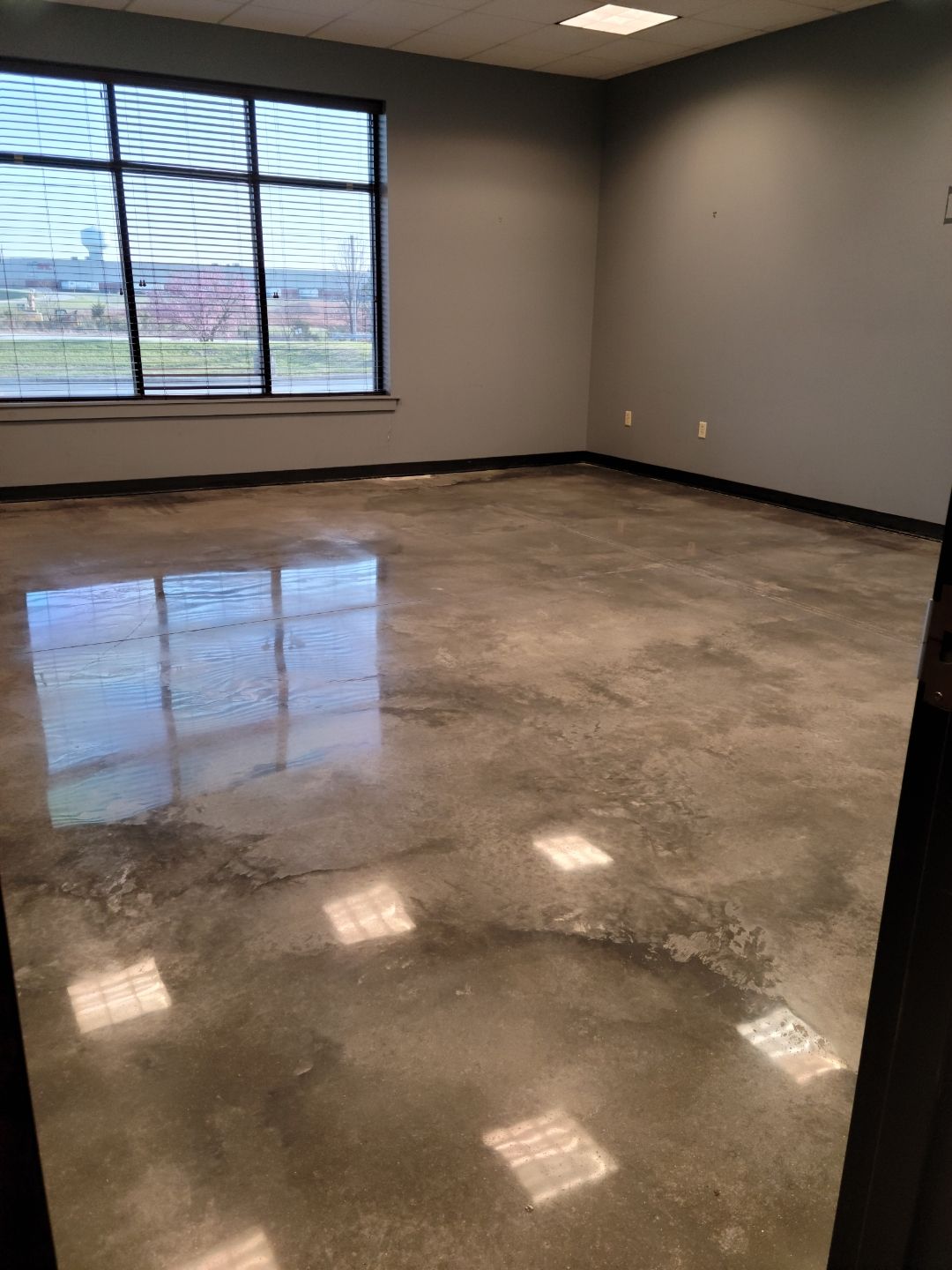 Empty room with polished concrete floor, gray walls, and large window.