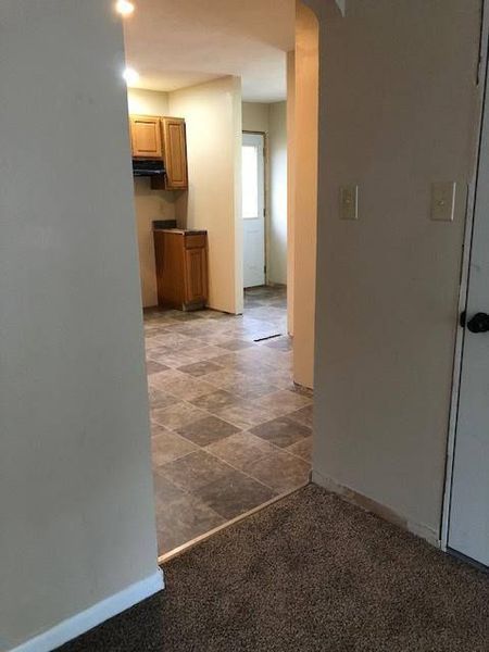 View from a room into a kitchen and hallway with linoleum flooring and a brown cabinet.