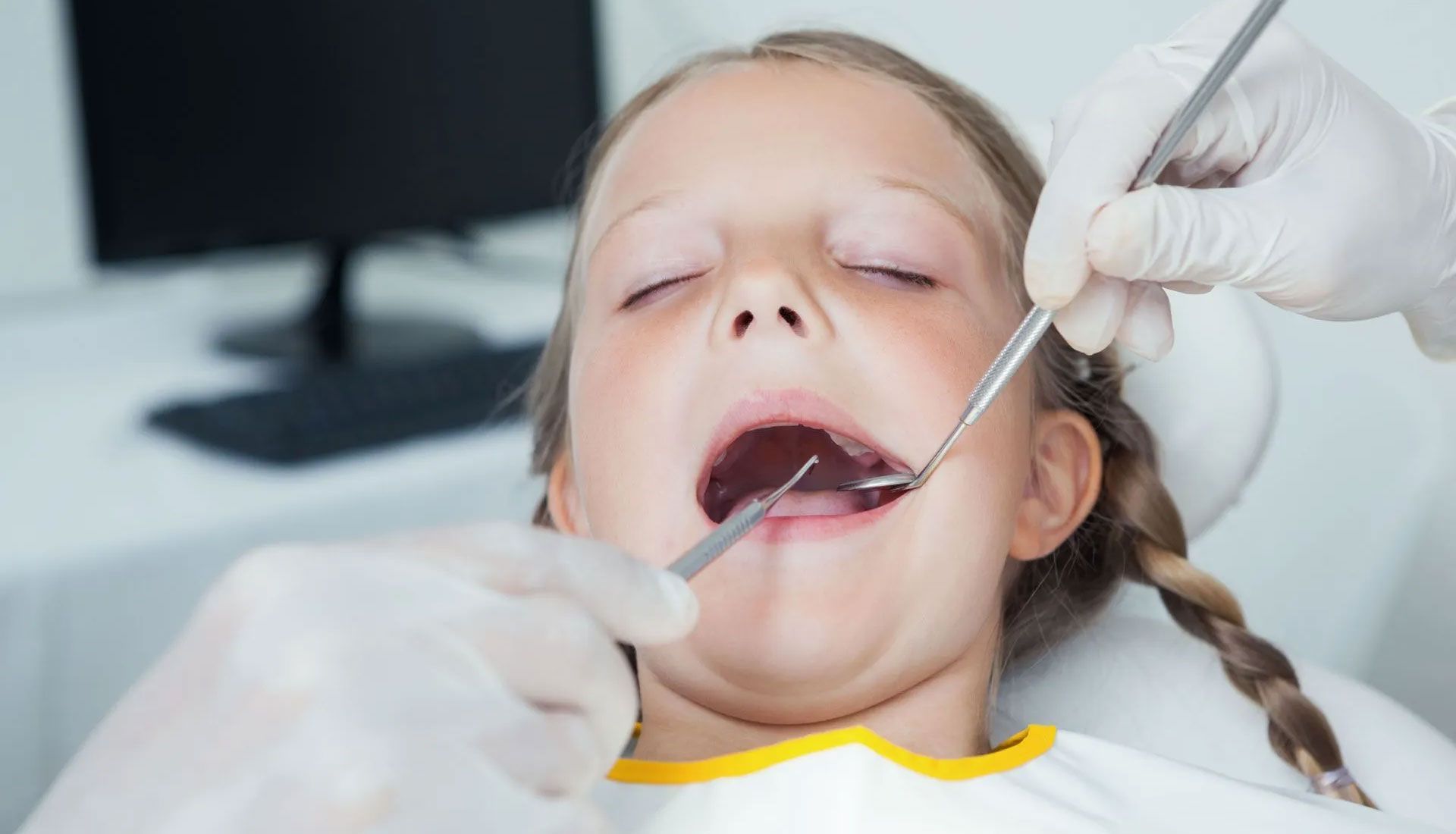 Dentist examining a child’s open mouth with dental tools while wearing gloves