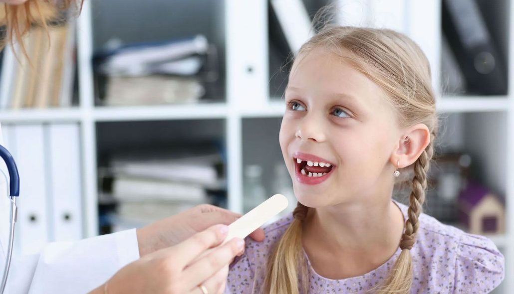 Girl smiling while a dentist holds a toothbrush near her mouth in a bright clinic waiting room