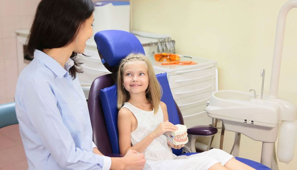 Dentist talking with smiling child patient in a dental exam chair