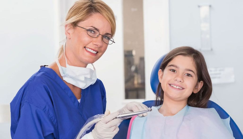 Dentist in blue scrubs holding a dental tool beside a smiling patient in a dental clinic.