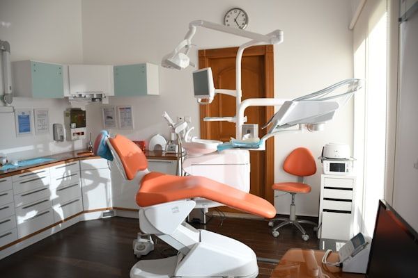 Modern dental exam room with orange chair, overhead light, cabinets, and sink