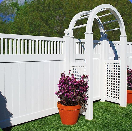 A white fence with purple flowers in pots next to it.