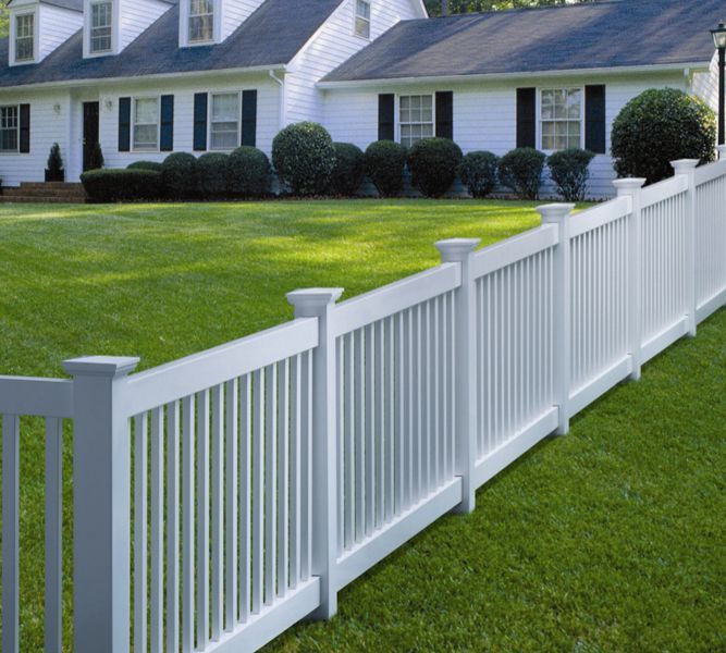 A white fence surrounds a lush green lawn in front of a house.