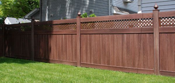A wooden fence surrounds a lush green lawn in front of a house.