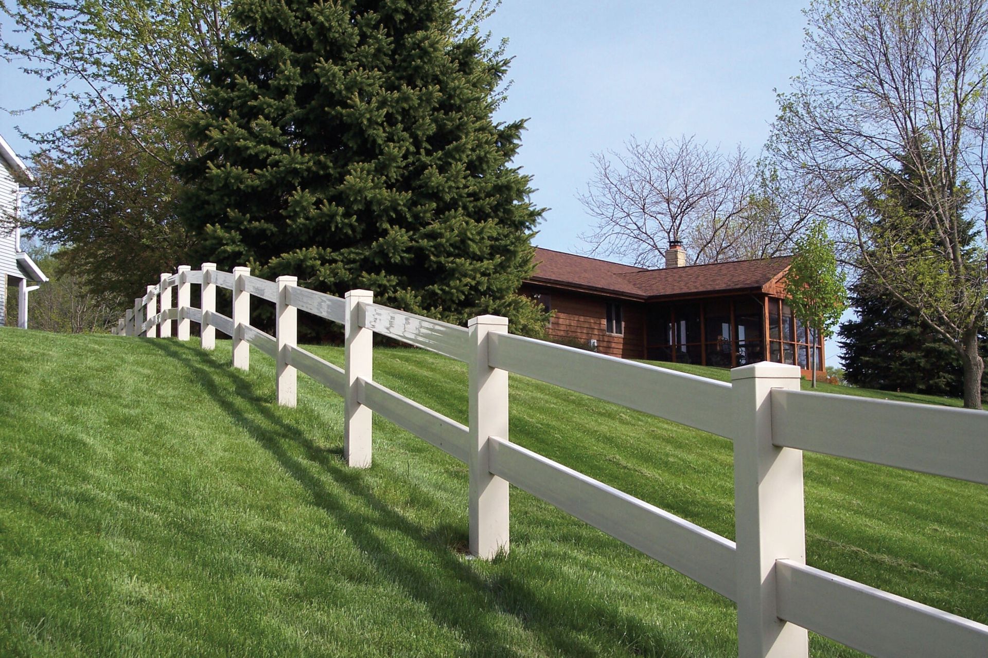 A white fence surrounds a lush green field in front of a house