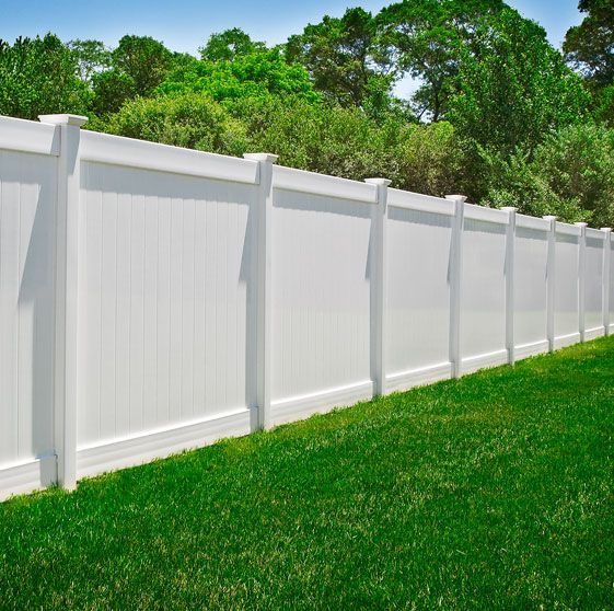A white fence surrounds a lush green lawn with trees in the background