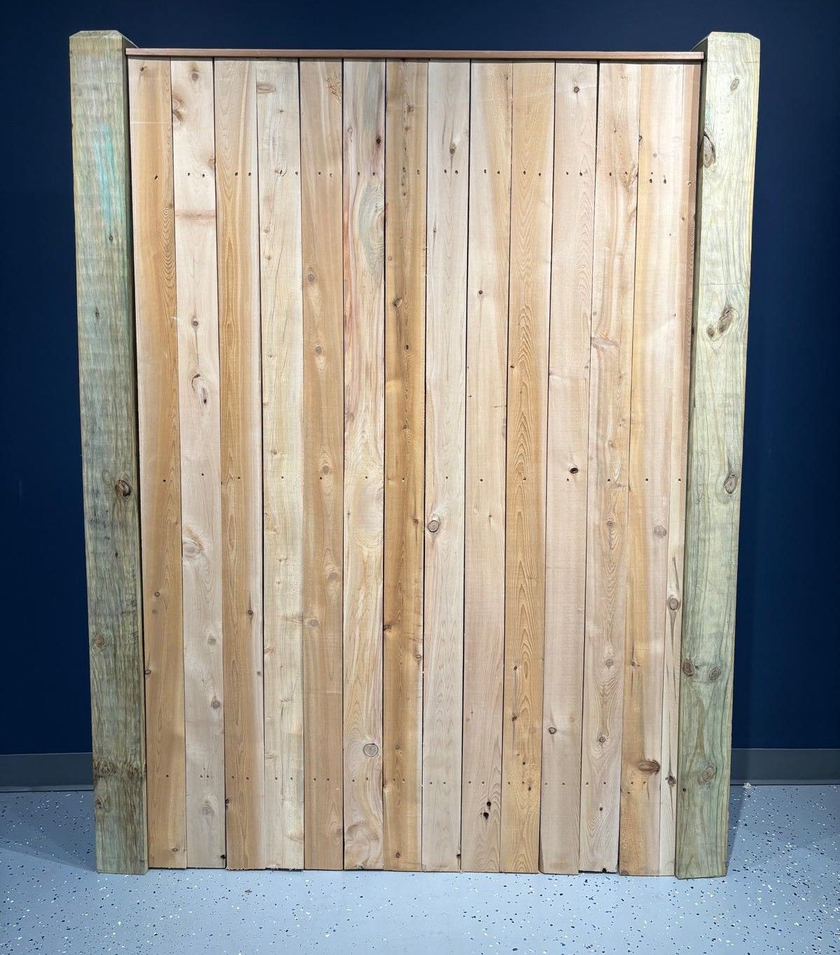 A wooden fence is sitting on a concrete floor in front of a blue wall.