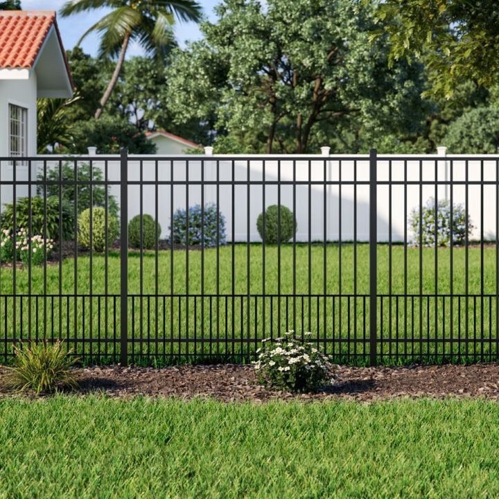 A black metal fence surrounds a lush green lawn in front of a house.