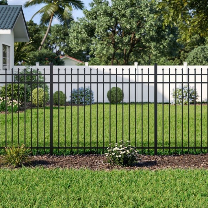 A black metal fence surrounds a lush green lawn in front of a house.