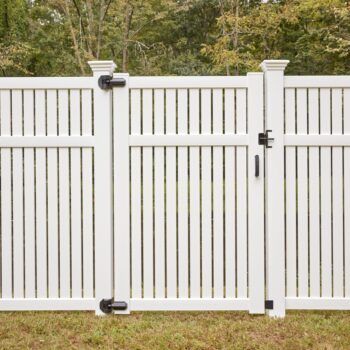 A white vinyl fence with a gate in the grass.
