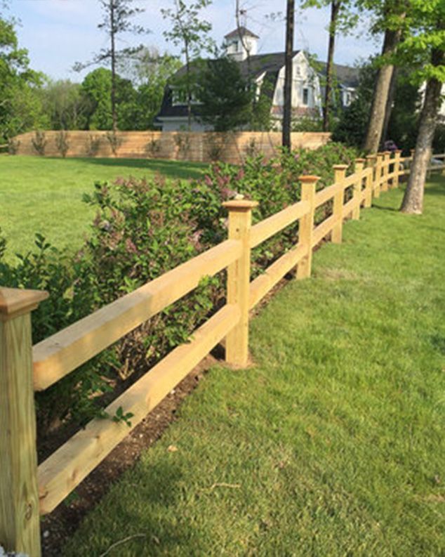 A wooden fence is in the middle of a lush green field.