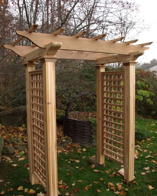 A wooden pergola is sitting in the middle of a lush green yard