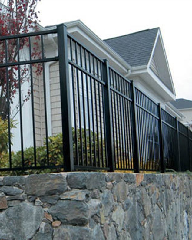 A black fence surrounds a stone wall in front of a house