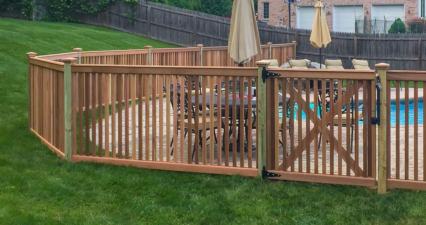 A wooden fence surrounds a swimming pool with chairs and umbrellas.