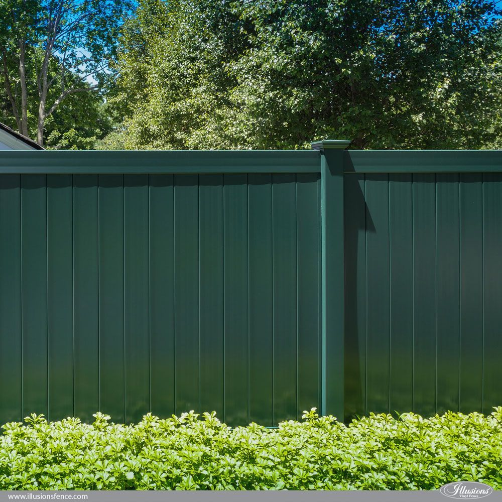 A green fence is surrounded by green bushes and trees.
