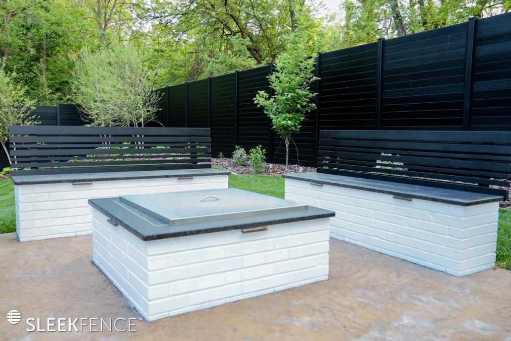 A patio with a fire pit and benches in front of a black fence.