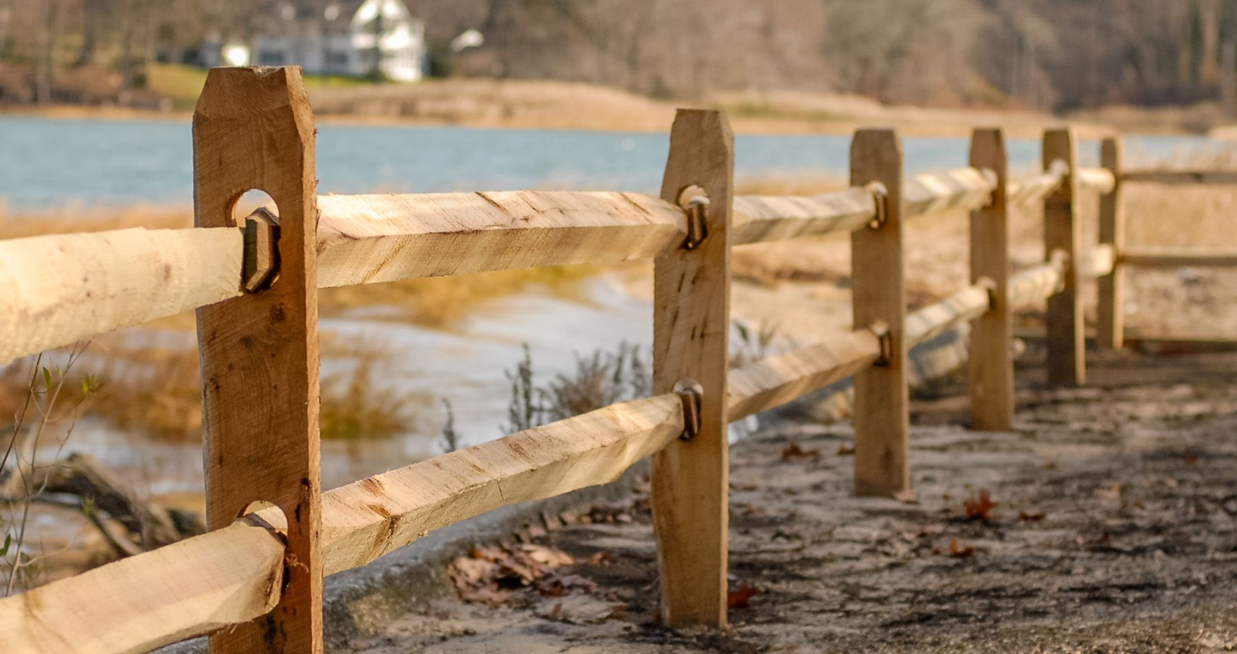 A wooden fence along a path next to a body of water.
