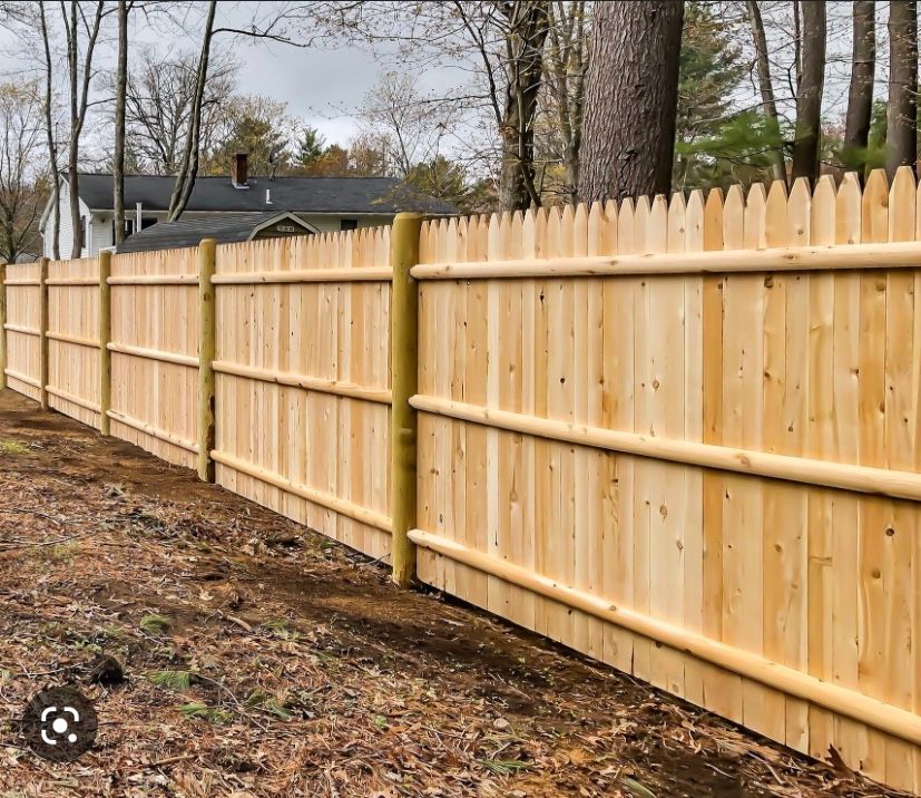 A wooden fence is surrounded by trees and a house in the background.