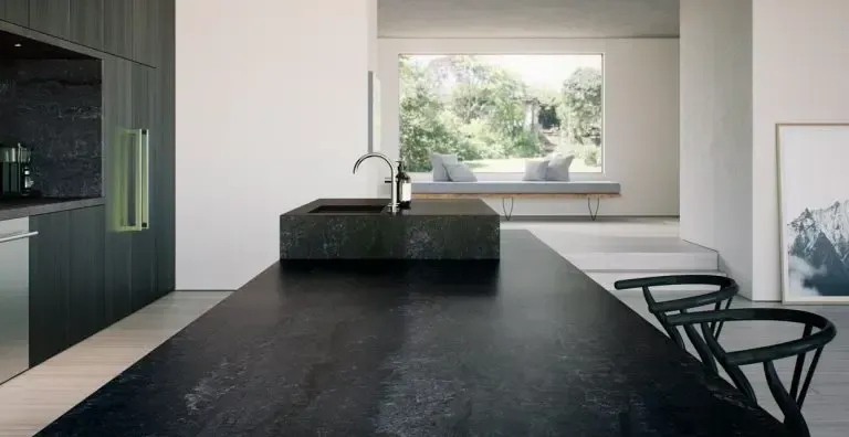 Modern kitchen with dark countertops, island sink, and large window overlooking trees.