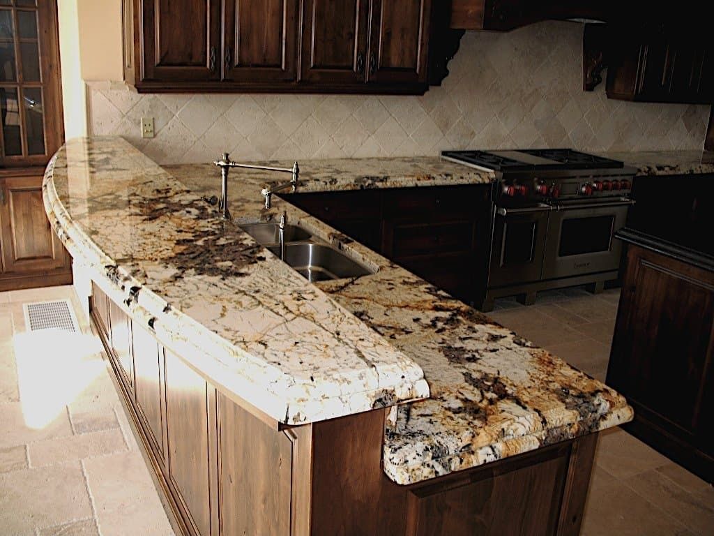 Granite countertop kitchen island with a built-in sink, brown cabinets, and stainless steel stove.