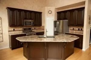 Brown kitchen with island, granite countertops, dark cabinets, stainless steel appliances.