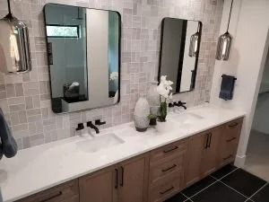 Bathroom with dual sinks, wood cabinets, two mirrors, neutral-colored tile, pendant lights, and white countertop.