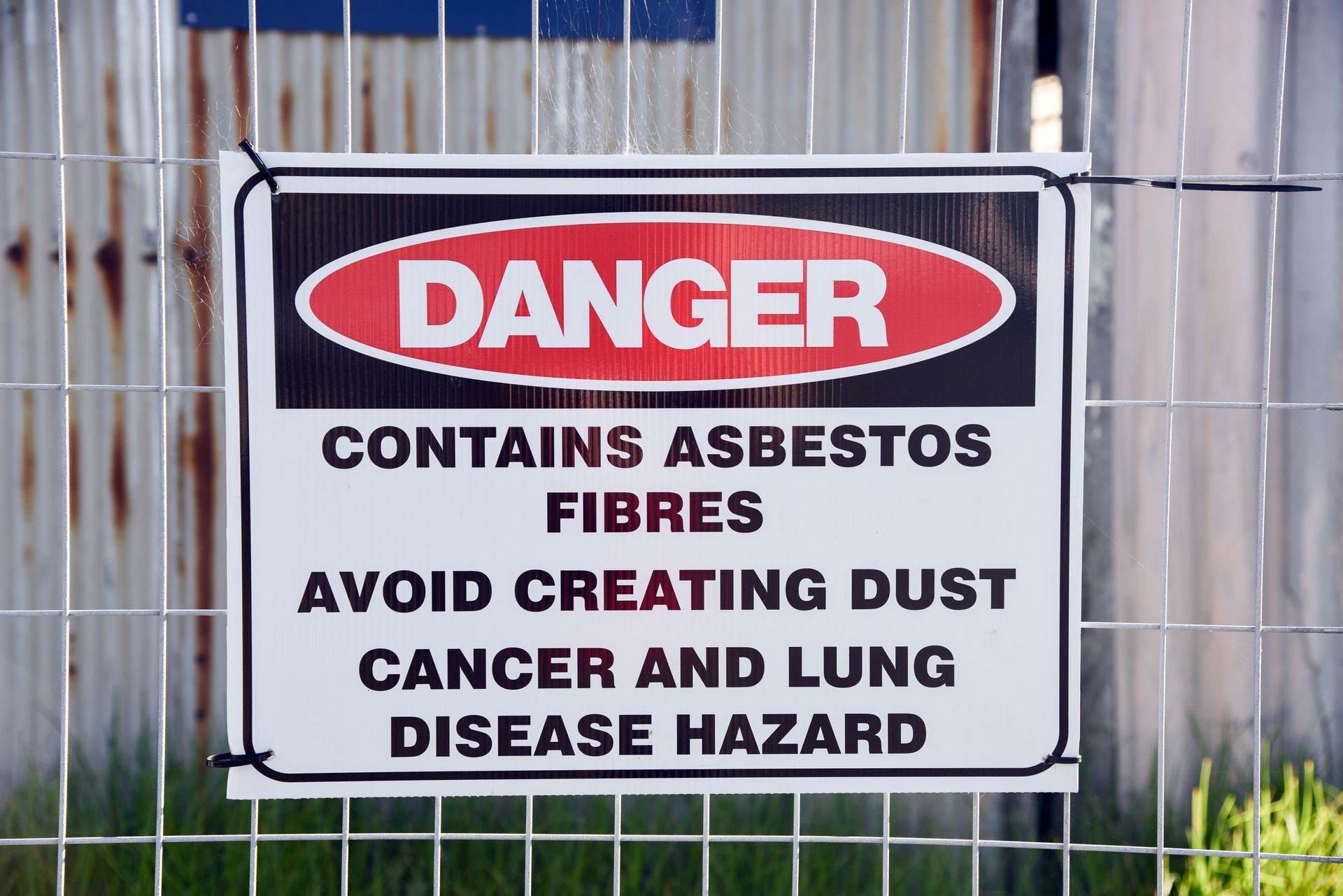 Danger sign: contains asbestos fibres, avoid creating dust, cancer and lung disease hazard, on a fence.