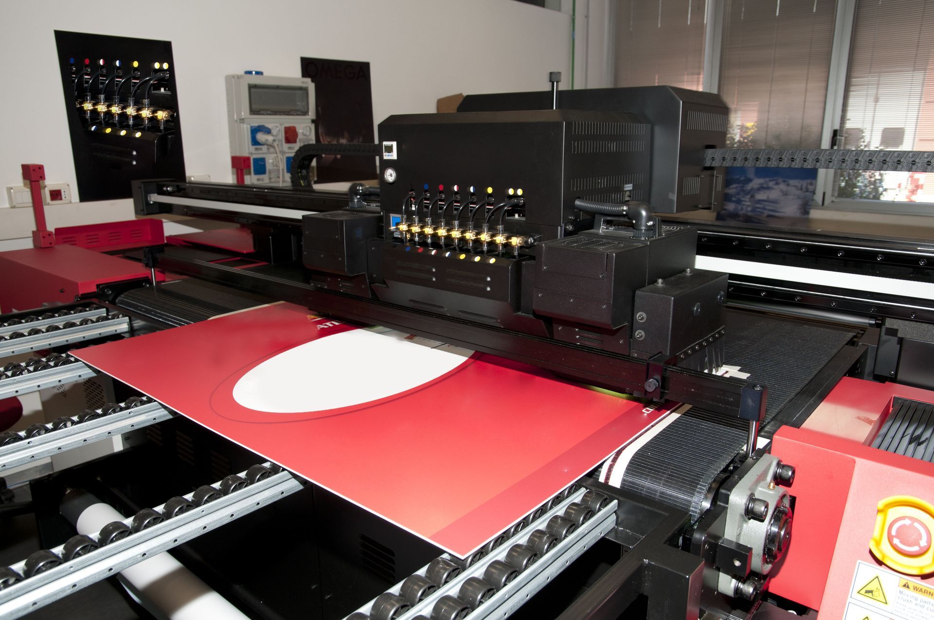 Large format printer printing a red and white design on a sheet of material.